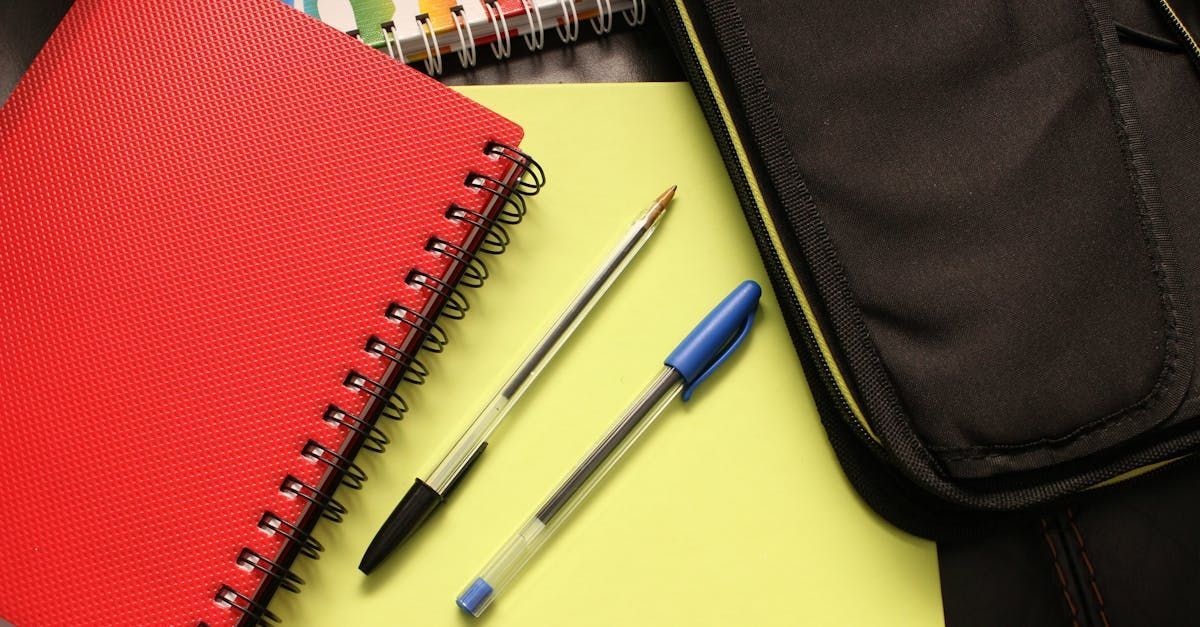 A notebook and two pens are on a table next to a black bag