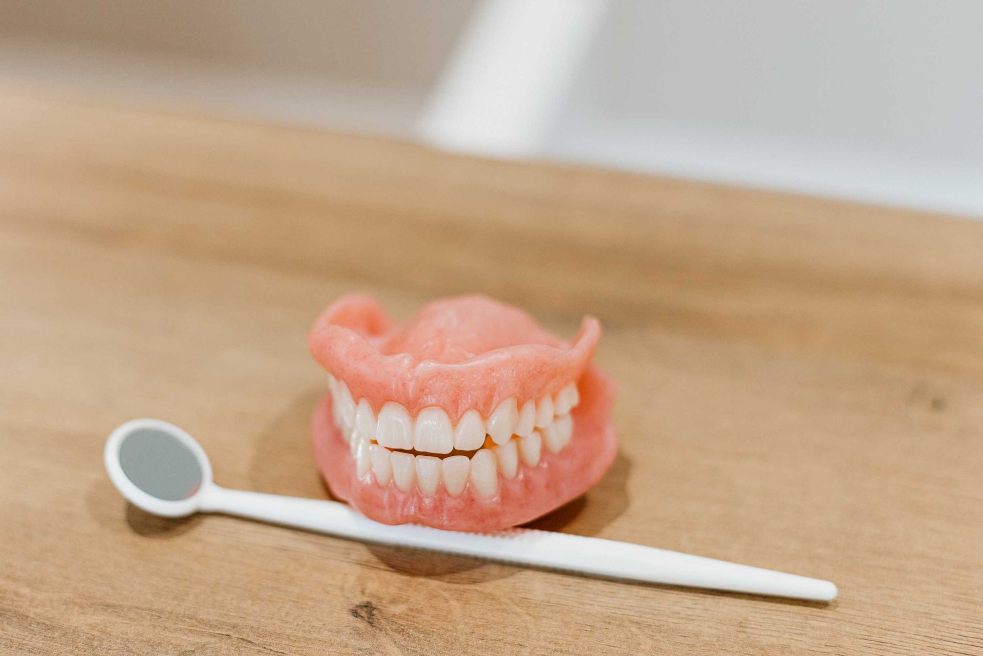 A Denture and a Dental Mirror Are on a Wooden Table — Harvey Smiles Denture Clinic In Burleigh Heads, QLD