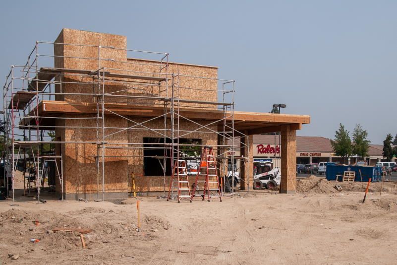 Construction site of a building; scaffolding surrounds wooden frame, partial signage visible.