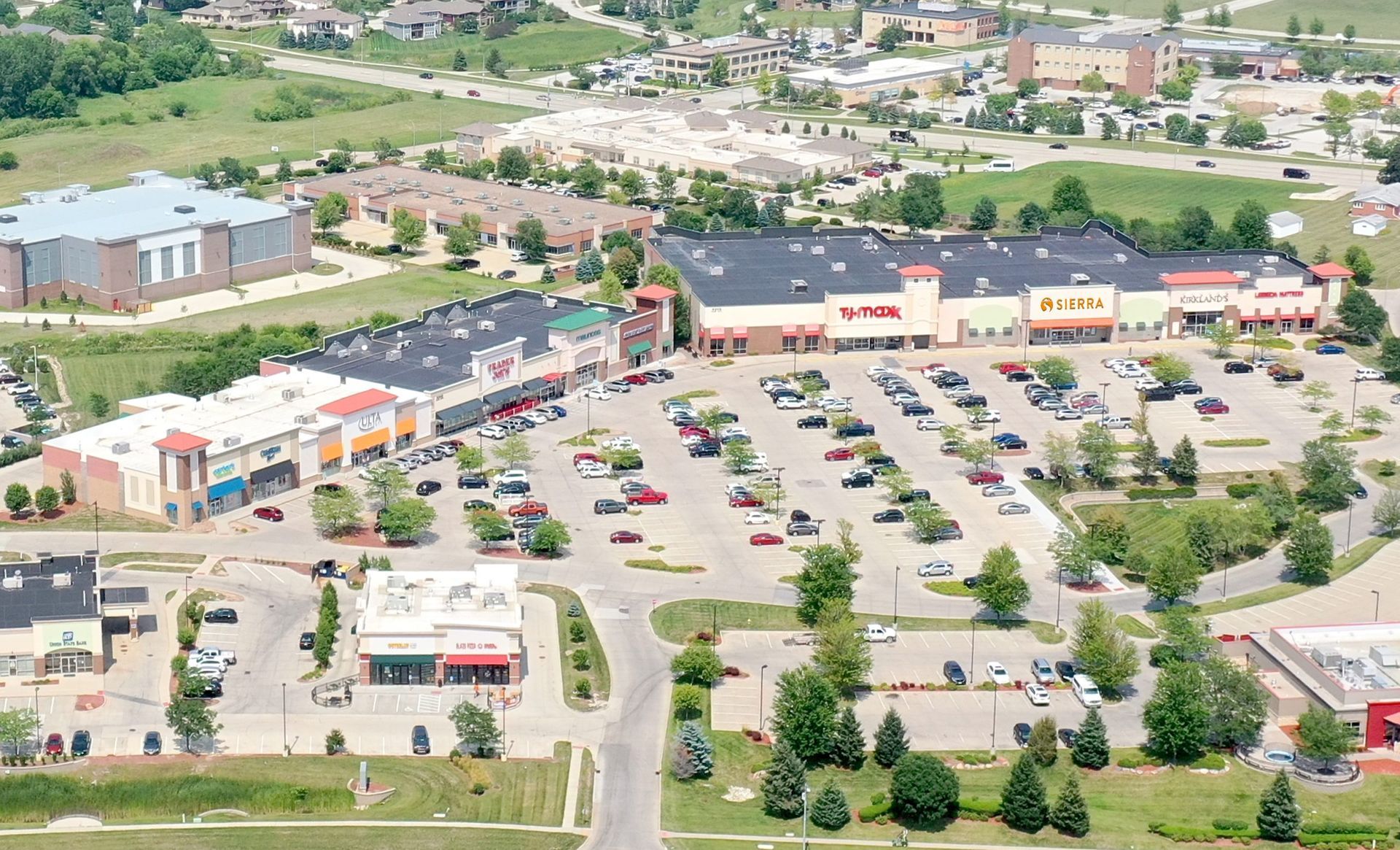 Aerial view of a shopping plaza with multiple stores, parking lot, and surrounding buildings.