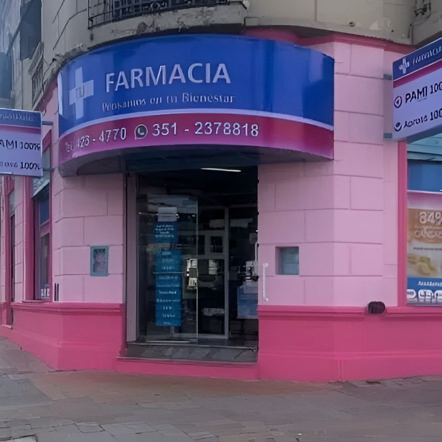 Fachada rosa de una farmacia con letrero azul y entrada de cristal en una acera de la ciudad.