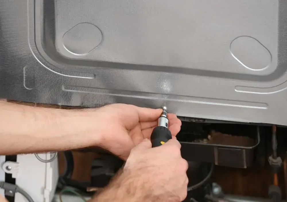 Hands Use a Screwdriver to Tighten a Metal Panel — Eurocoast Appliance Service In Woy Woy, NSW