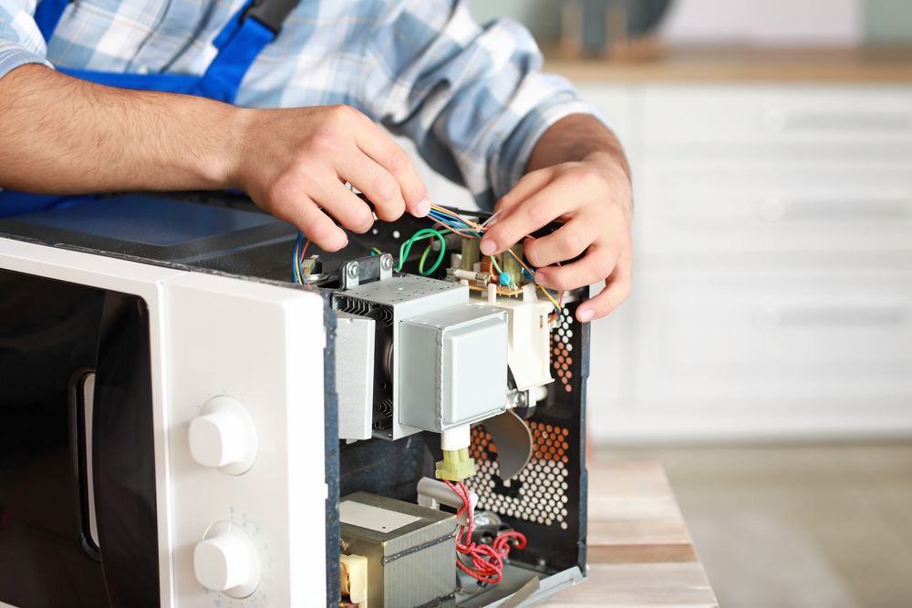 A Person Repairs the Internal Components of an Open Microwave — Eurocoast Appliance Service In Tuggerah, NSW