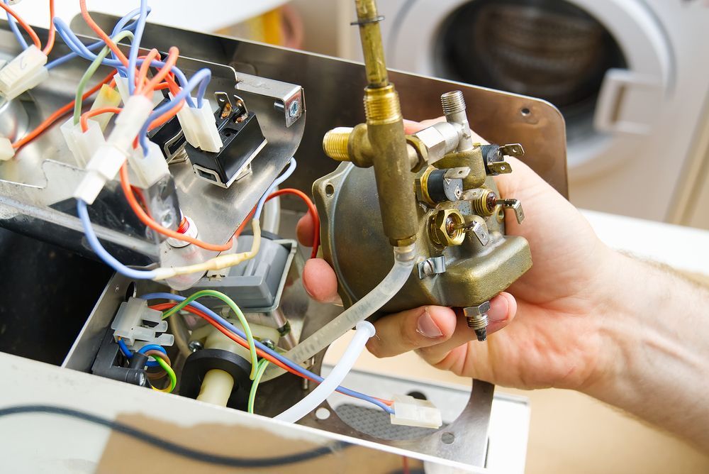 Person's Hand Holding a Brass-coloured Solenoid Valve — Eurocoast Appliance Service In Bateau Bay, NSW