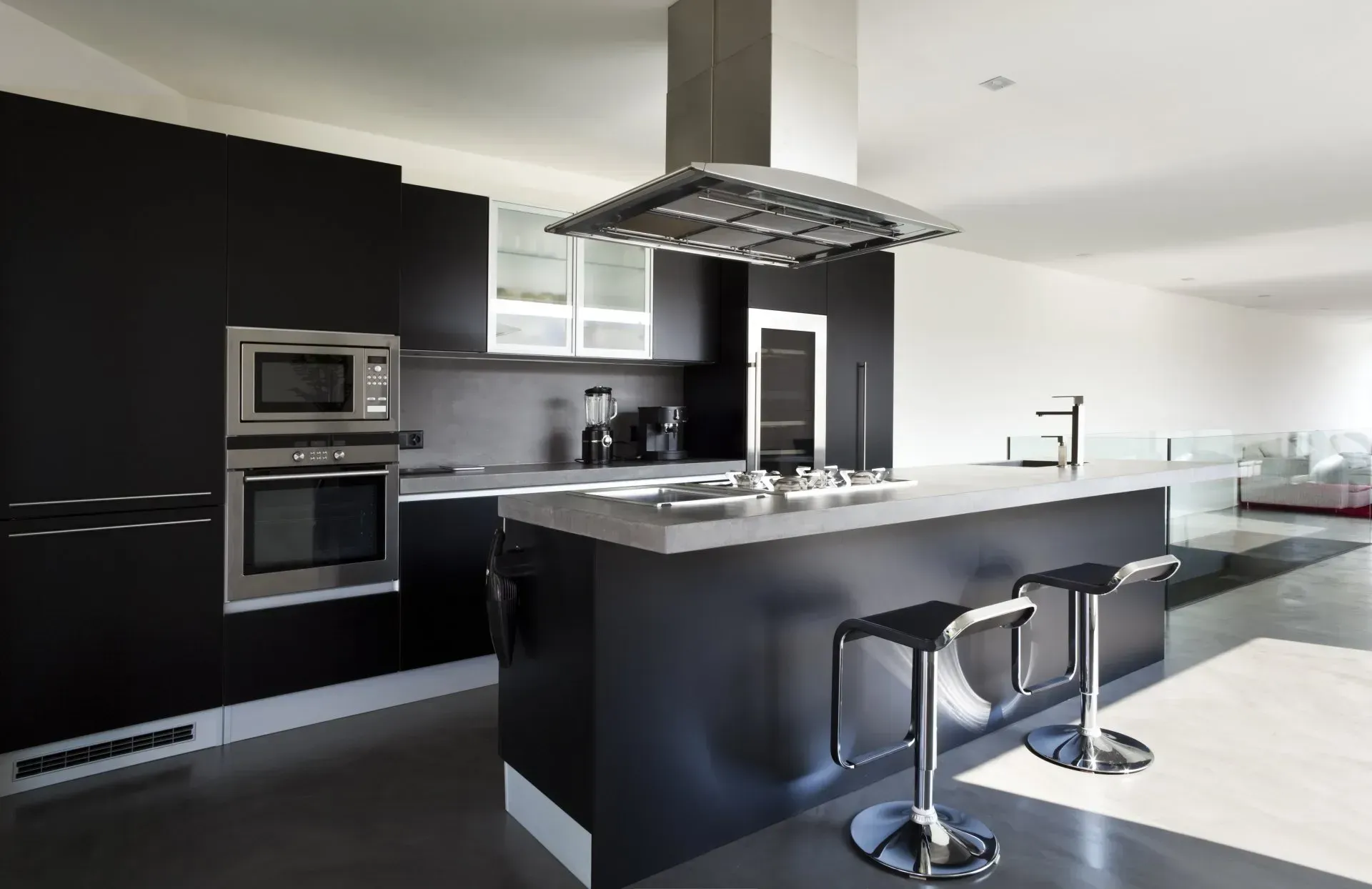A modern kitchen featuring black cabinetry, a large kitchen island with two stools, stainless steel appliances, and a vent.— Eurocoast Appliance Service In Tuggerah, NSW