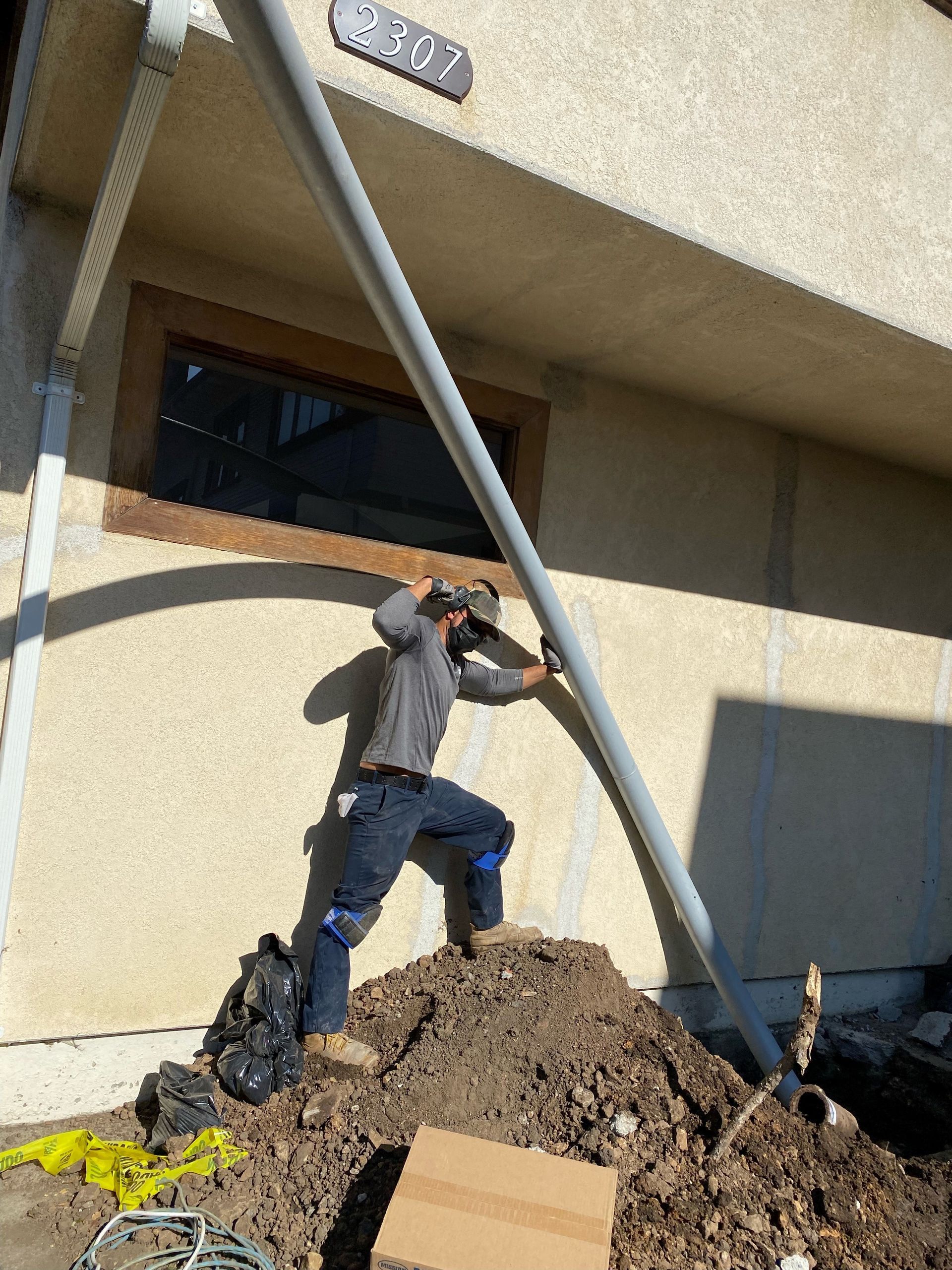 A man is working on a pipe outside of a building