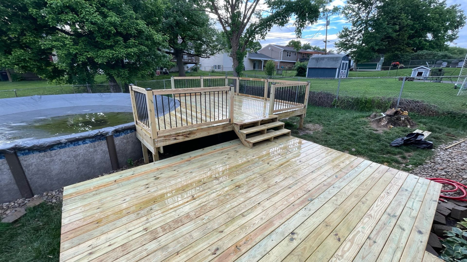 A wooden deck is sitting next to a pool in a backyard.