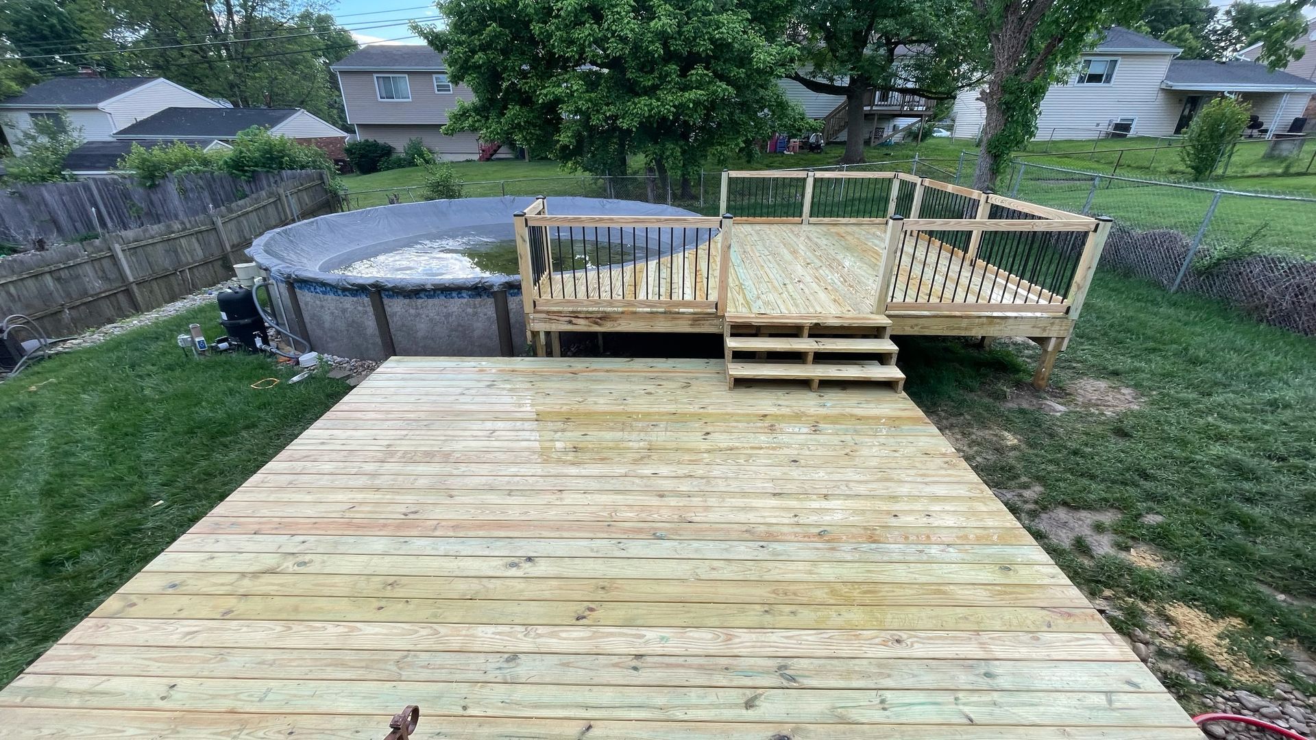 A wooden deck is sitting next to a pool in a backyard.