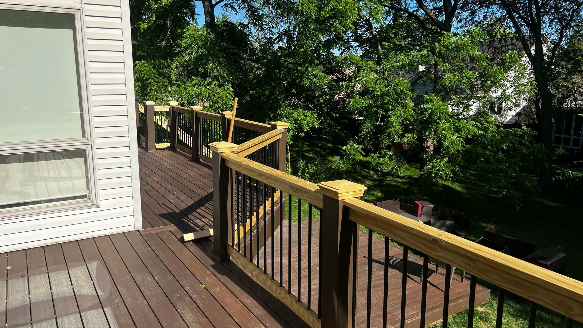 Wooden deck with dark brown planks, black railings, and green trees in the background.