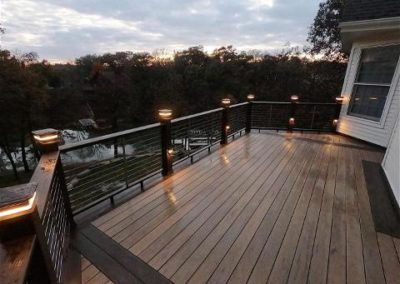 A large wooden deck with a railing and lights on it.