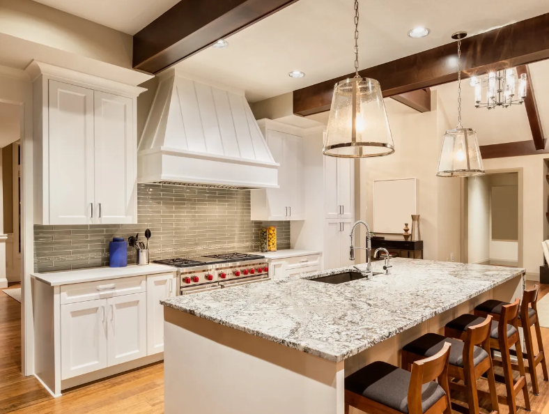 A kitchen with white cabinets , granite counter tops , a stove , sink , and stools.