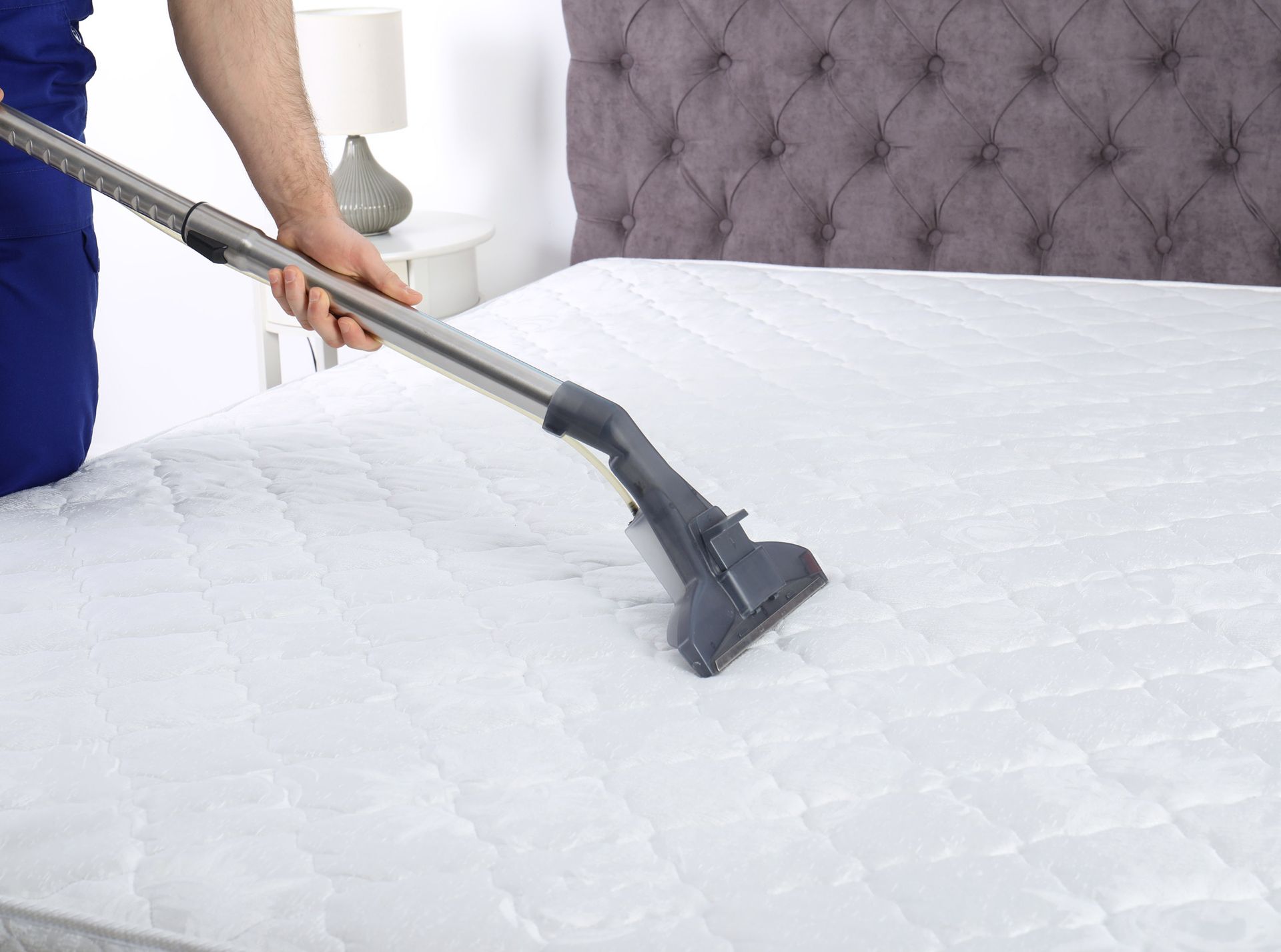 A person is cleaning a mattress with a vacuum cleaner.