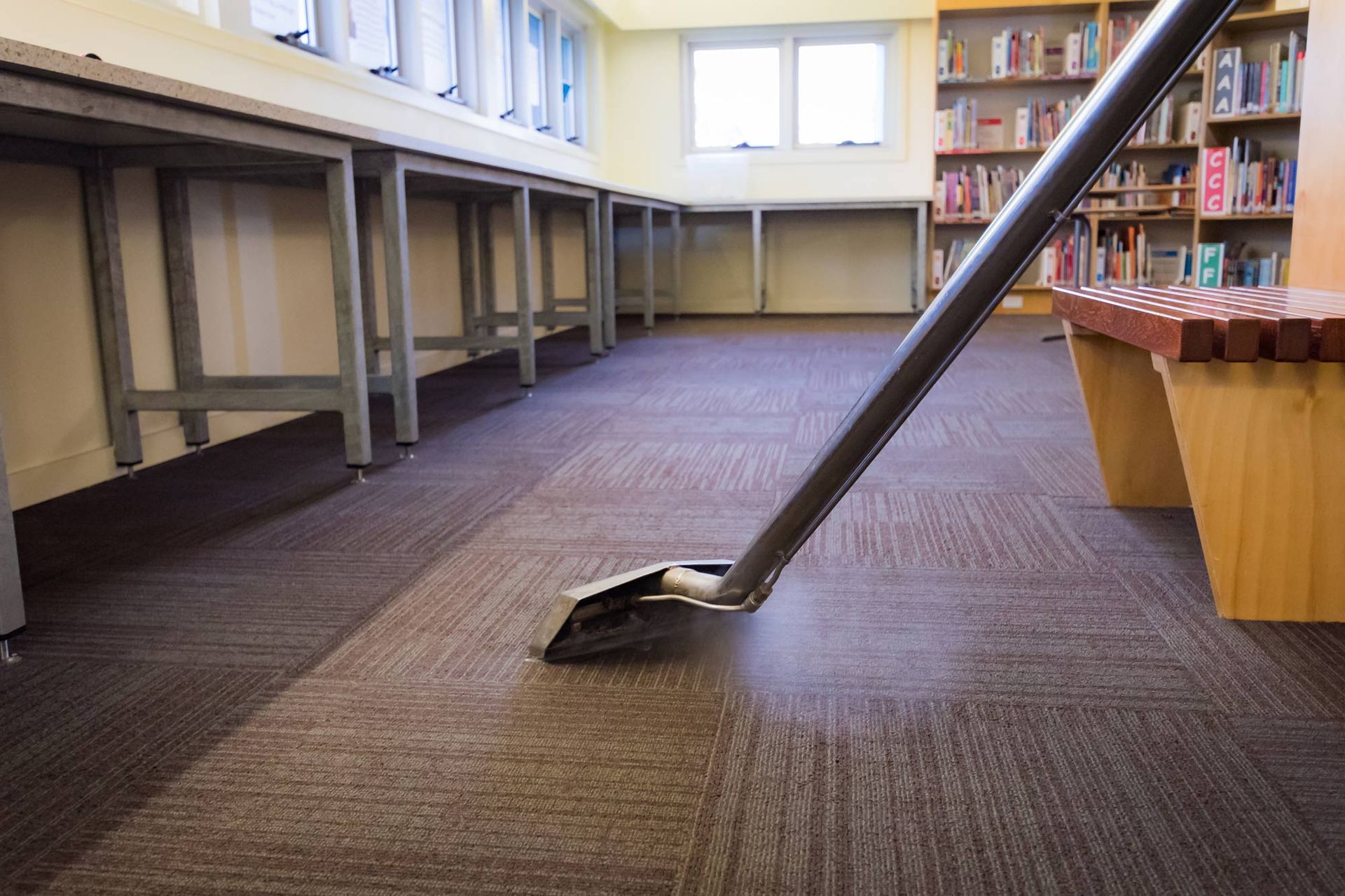 A vacuum cleaner is cleaning a carpeted floor in a library.