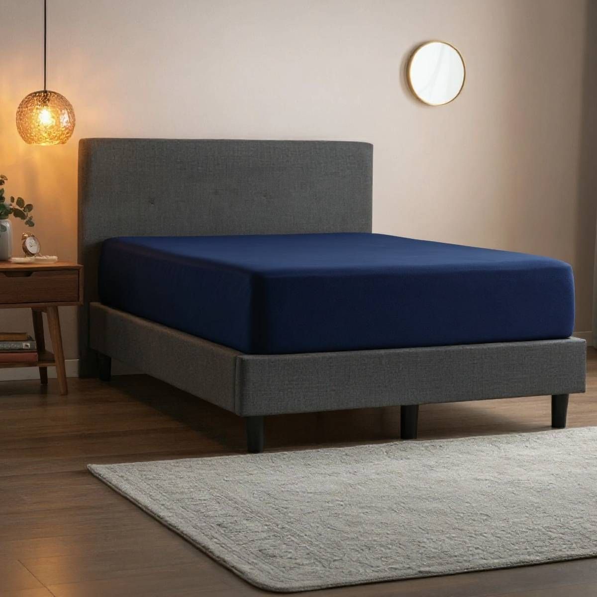 Navy blue fitted sheet on a gray bed in a softly lit bedroom with a rug and side table.