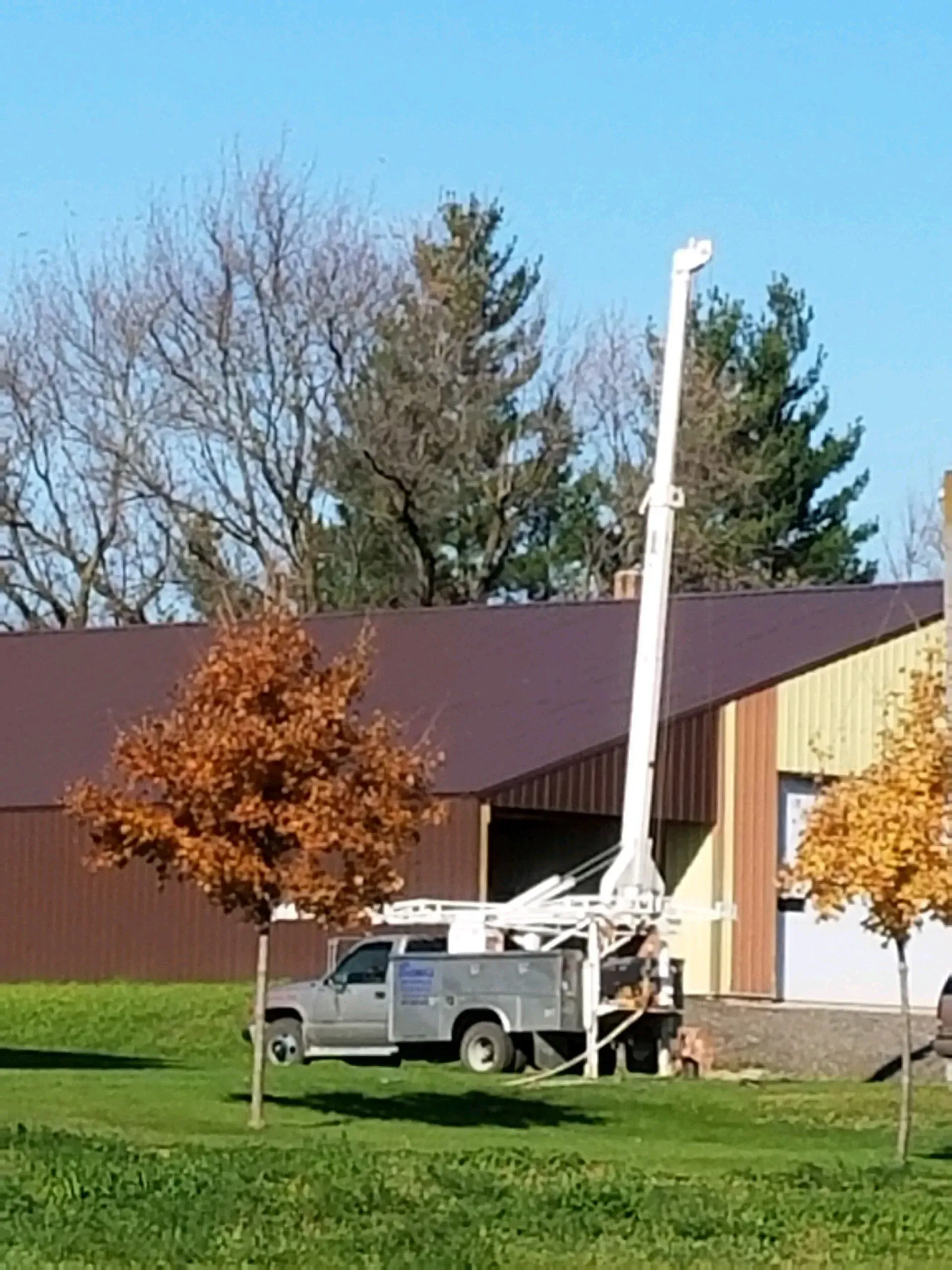 A white bucket truck with its arm extended stands in front of a building with a brown roof.