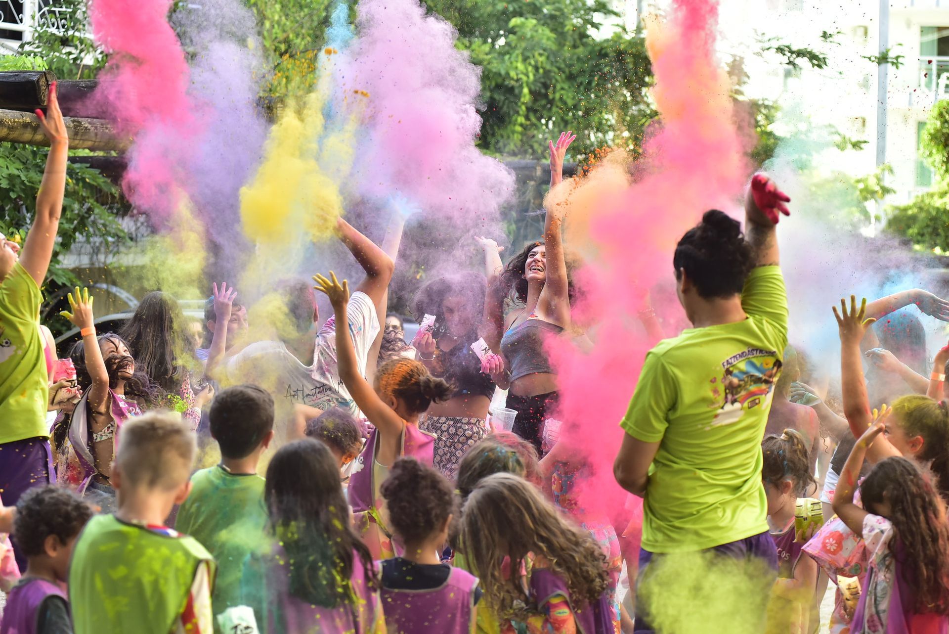 Multidão de pessoas jogando pó colorido rosa, amarelo e verde ao ar livre em um festival de cores.