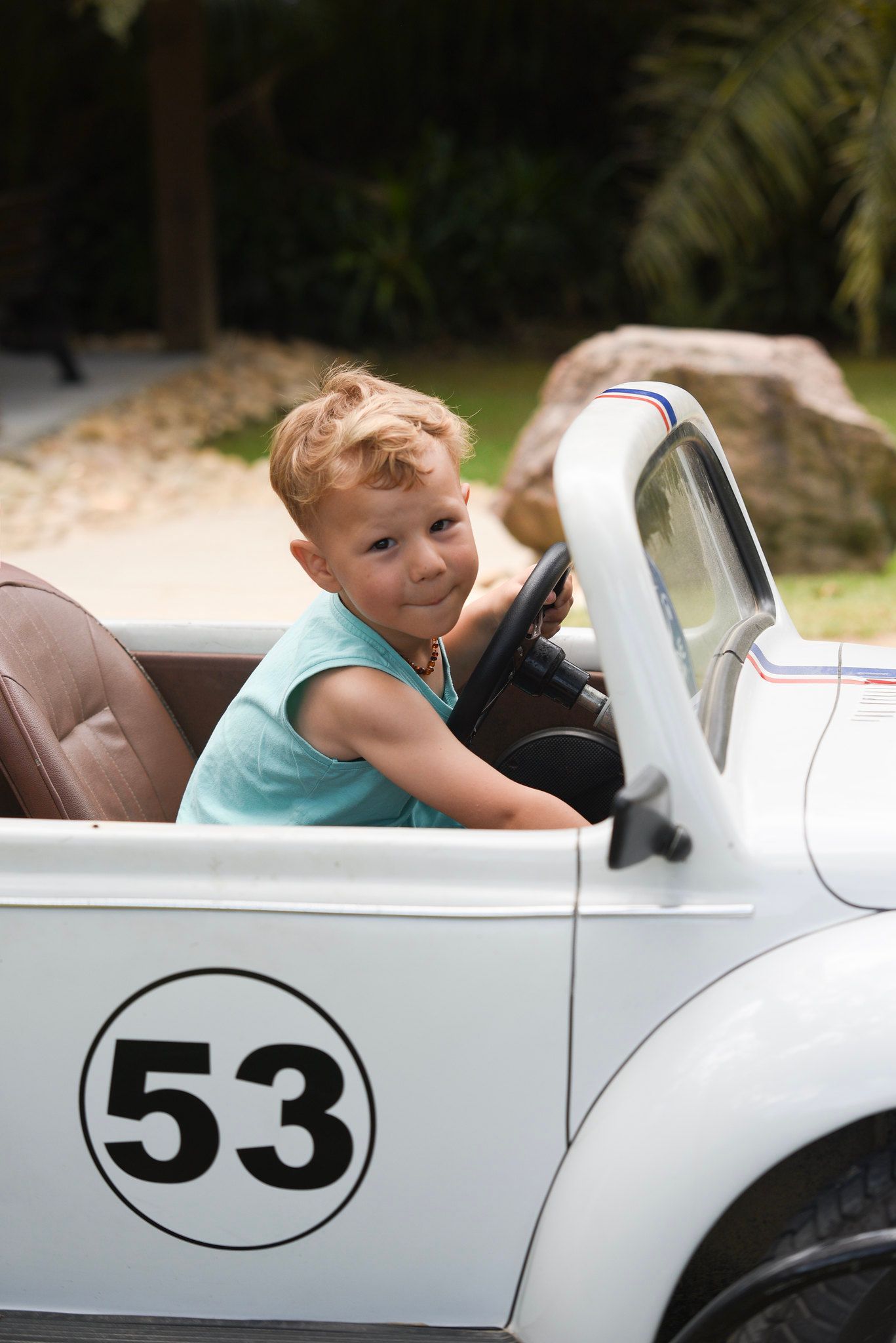 Criança sentada em um carro de corrida branco, número 53, sorrindo ao volante.