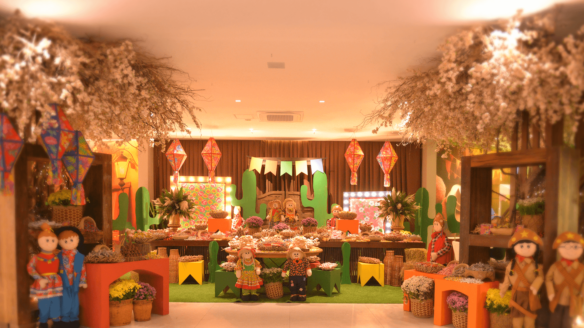 Arranjo floral festivo em ambiente interno com lanternas, cadeiras laranja e bonecas dispostas ao redor de uma mesa central decorada.