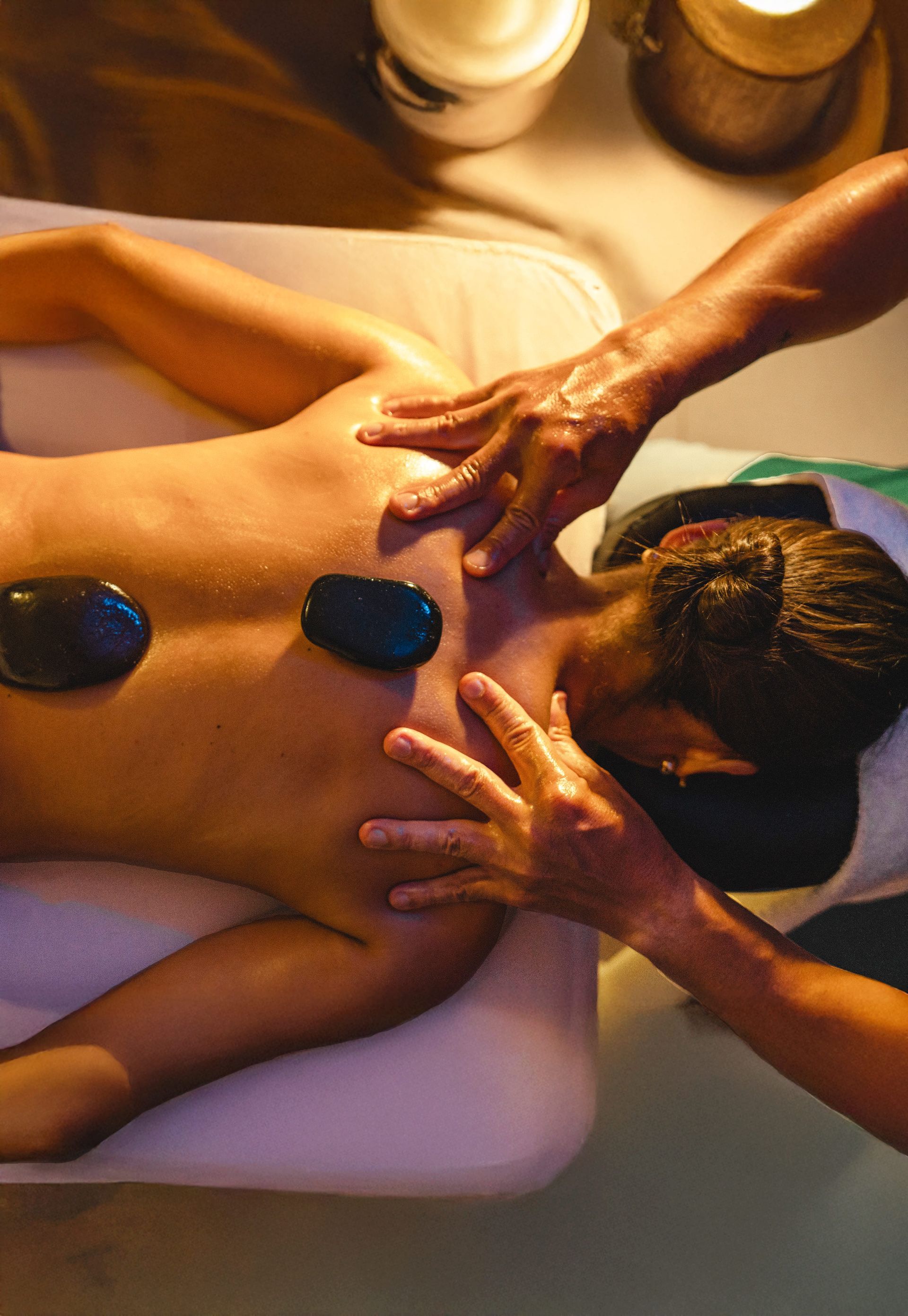 Massagista aplicando massagem nas costas com pedras quentes em uma maca de spa.