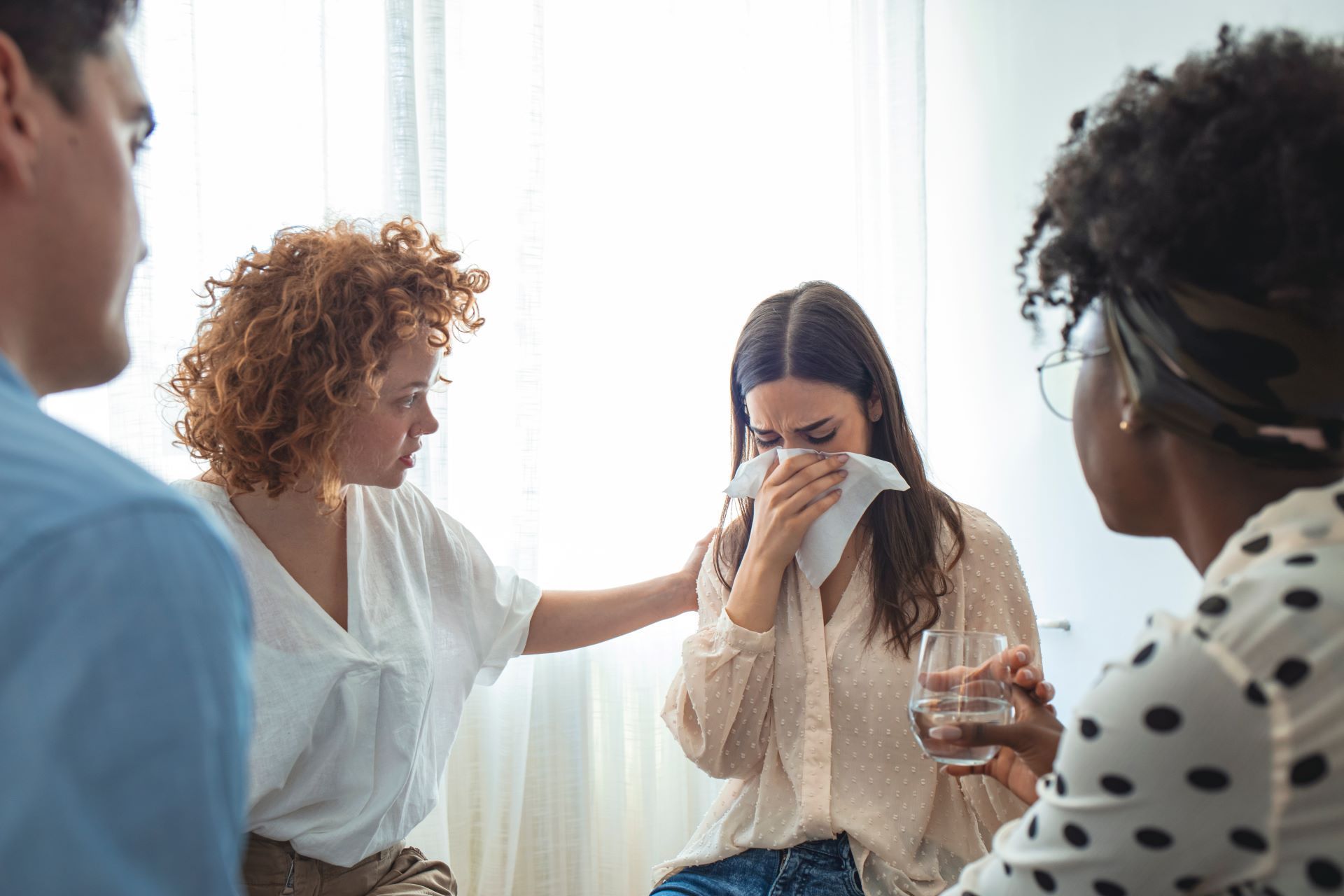 Group therapy session: woman crying, comforted by another; others offer support.