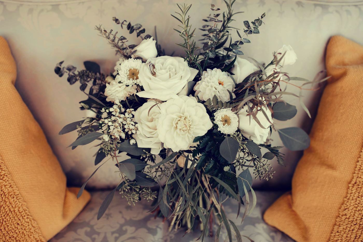 Bouquet of white flowers with green foliage on a couch flanked by yellow pillows.