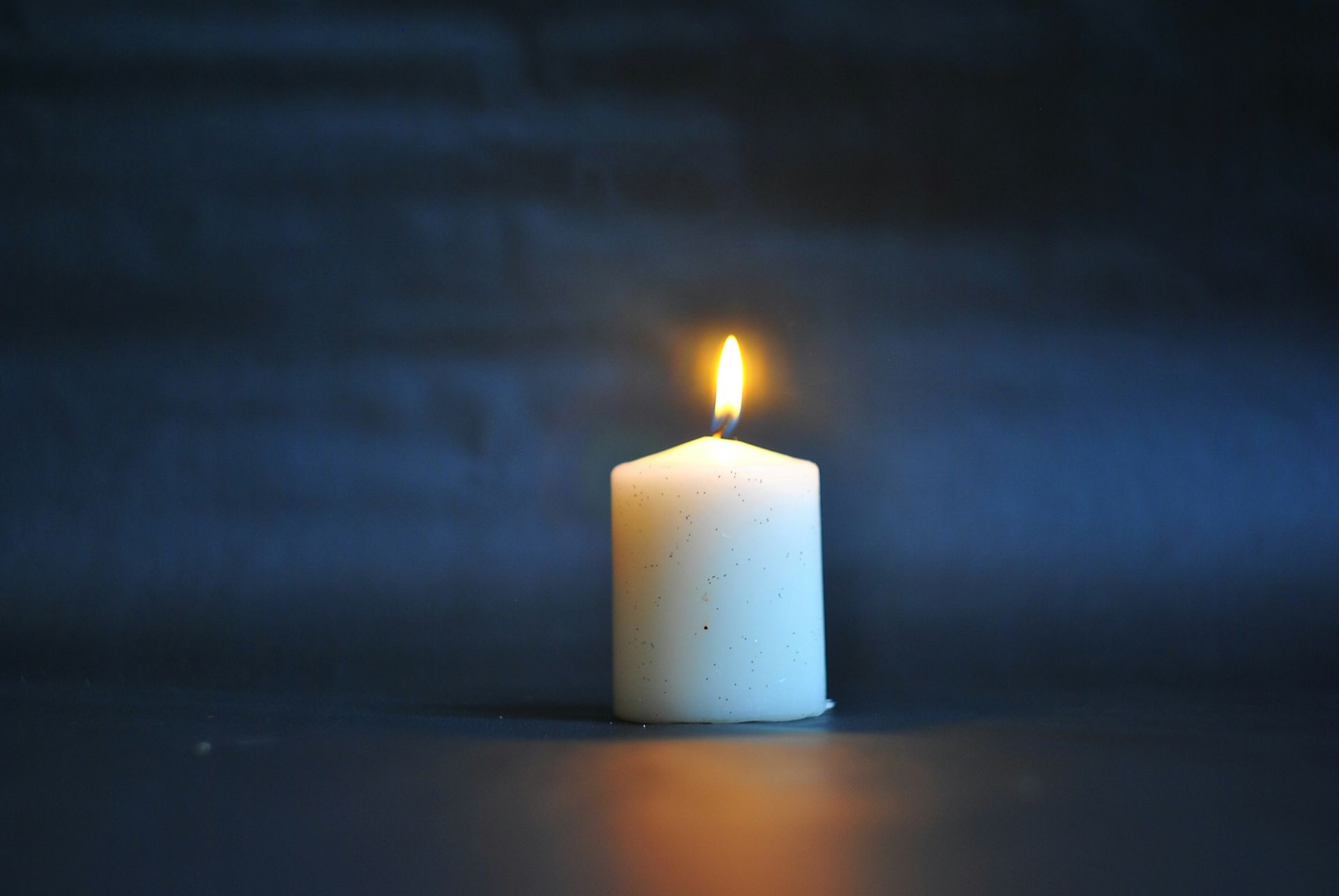 Lit white candle against a dark blue background.