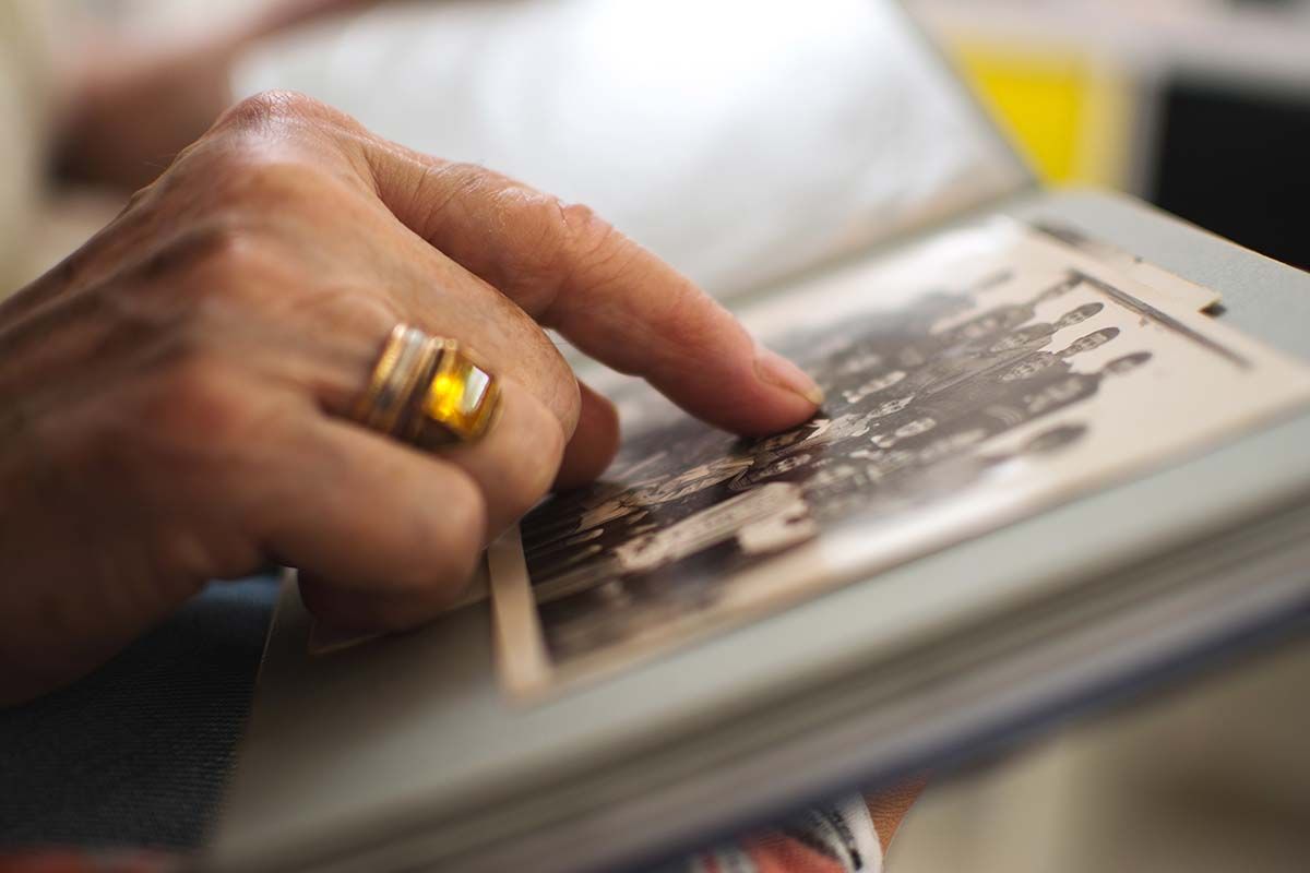 Hand with gold ring points at a black and white photograph in an album.