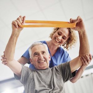 A woman is helping an elderly man with a resistance band – Andover, MA - At Home Care