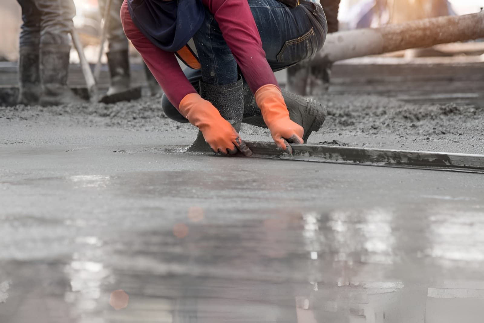 A Construction Worker is Kneeling Down and Spreading Concrete on the Ground — Tiga's Concreting Services In Branyan, QLD