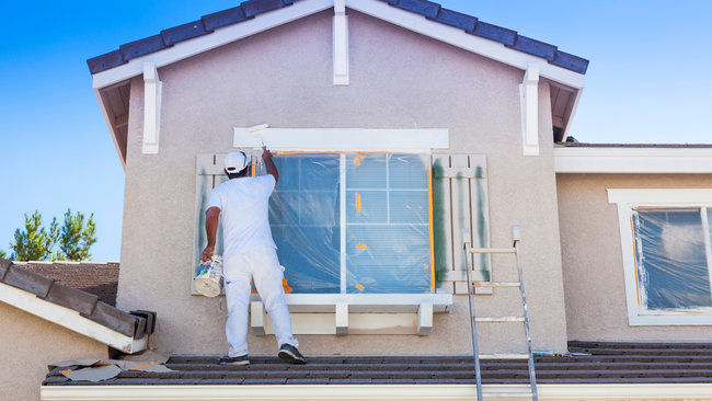 A man is painting a window on the side of a house.