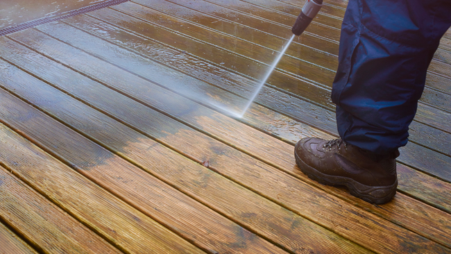 A person is cleaning a wooden deck with a high pressure washer.
