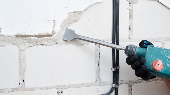 A person is using a hammer to drill a hole in a brick wall.