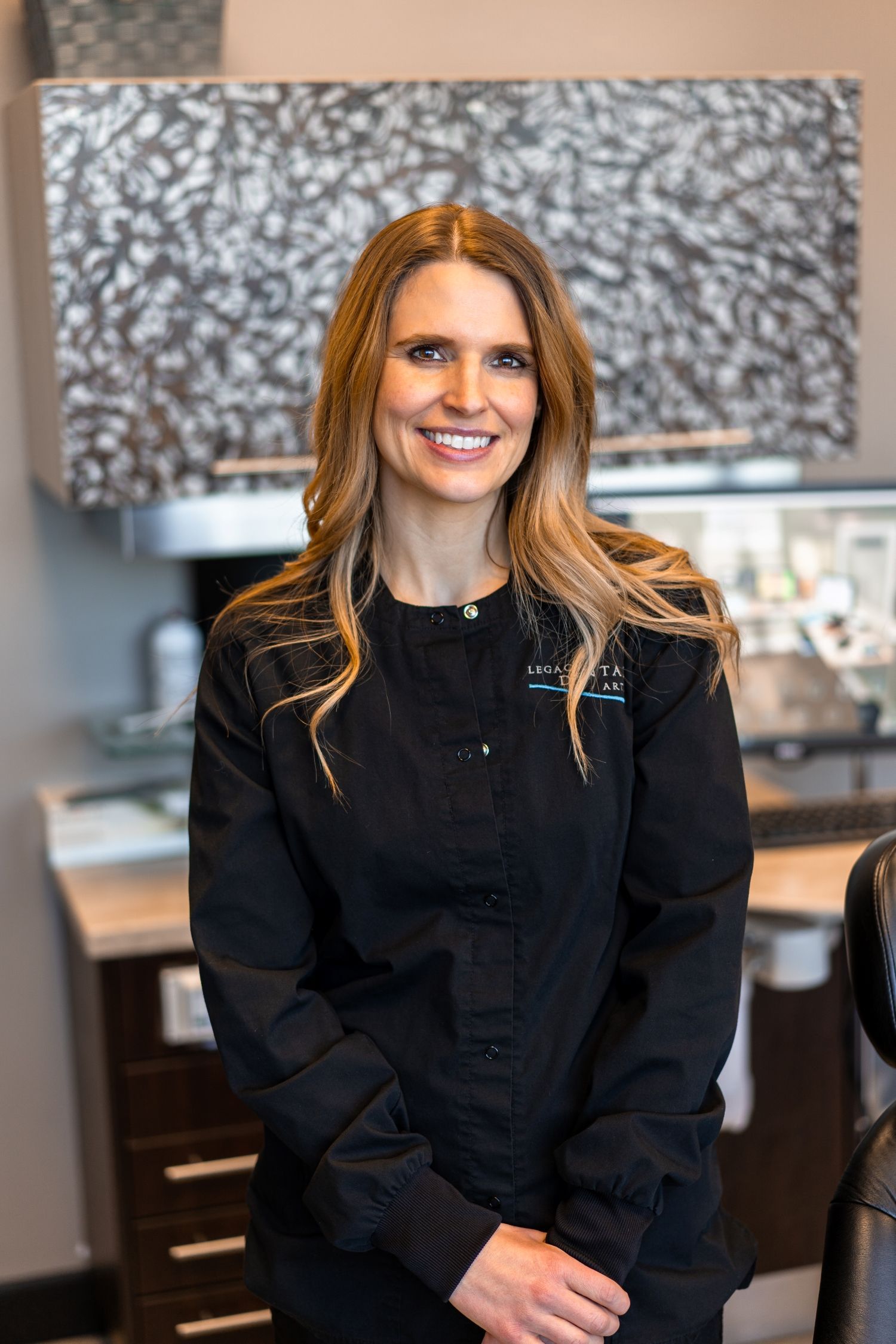 Woman in black scrubs smiles in a dental office.