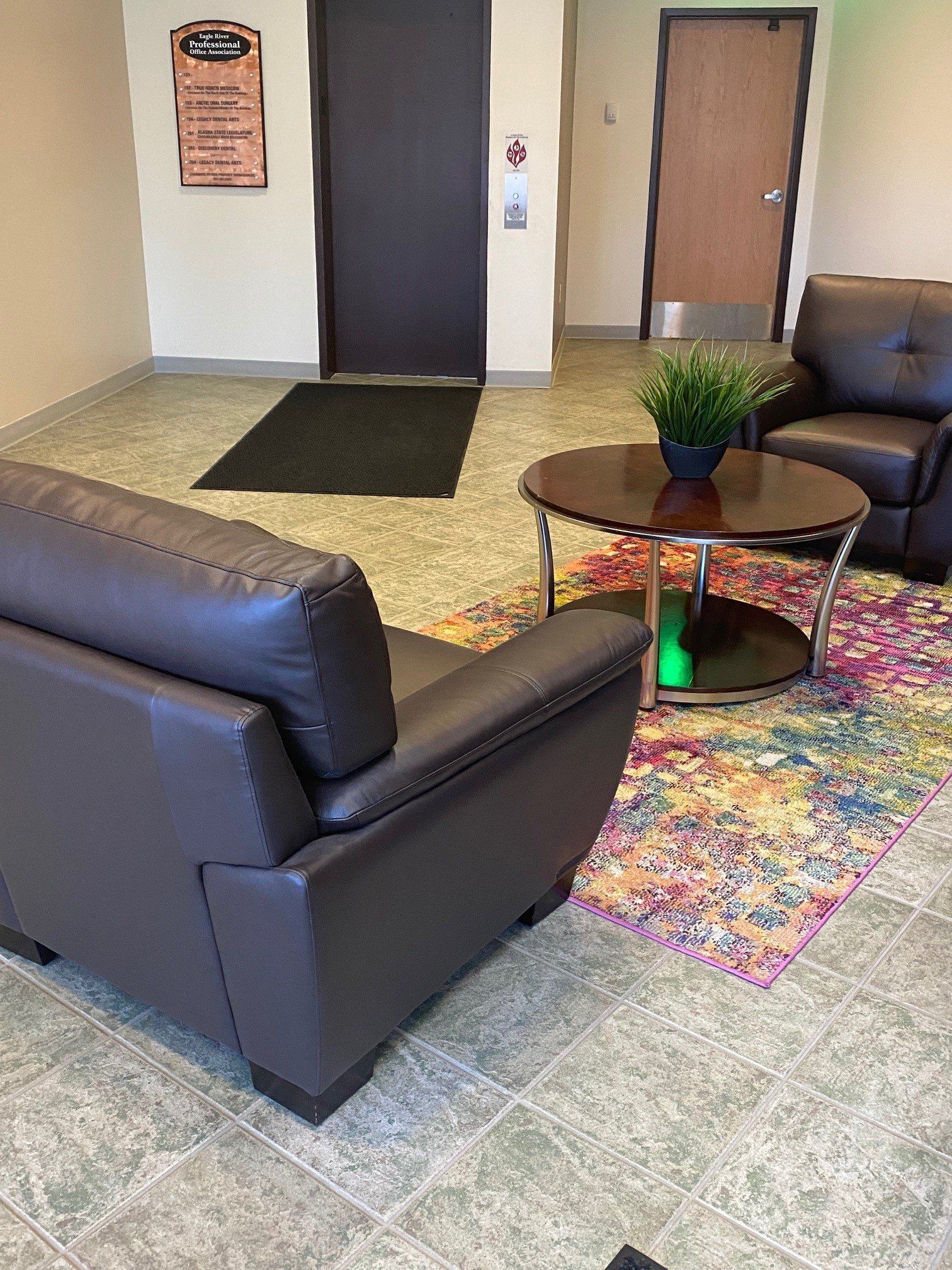 Lounge area with dark brown chairs, round table, colorful rug, and two doors.
