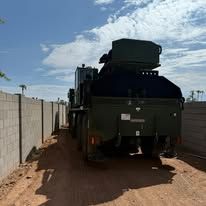 Green military vehicle parked next to a concrete wall, in an outdoor setting.