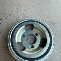 Metal car engine pulley with three holes and a black rubber ring, on a gray surface.