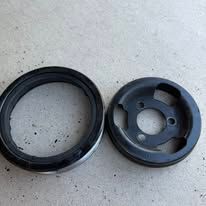 Two black metal car parts: a circular ring and a pulley with three holes.