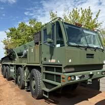 Green military truck with large tires parked outdoors.