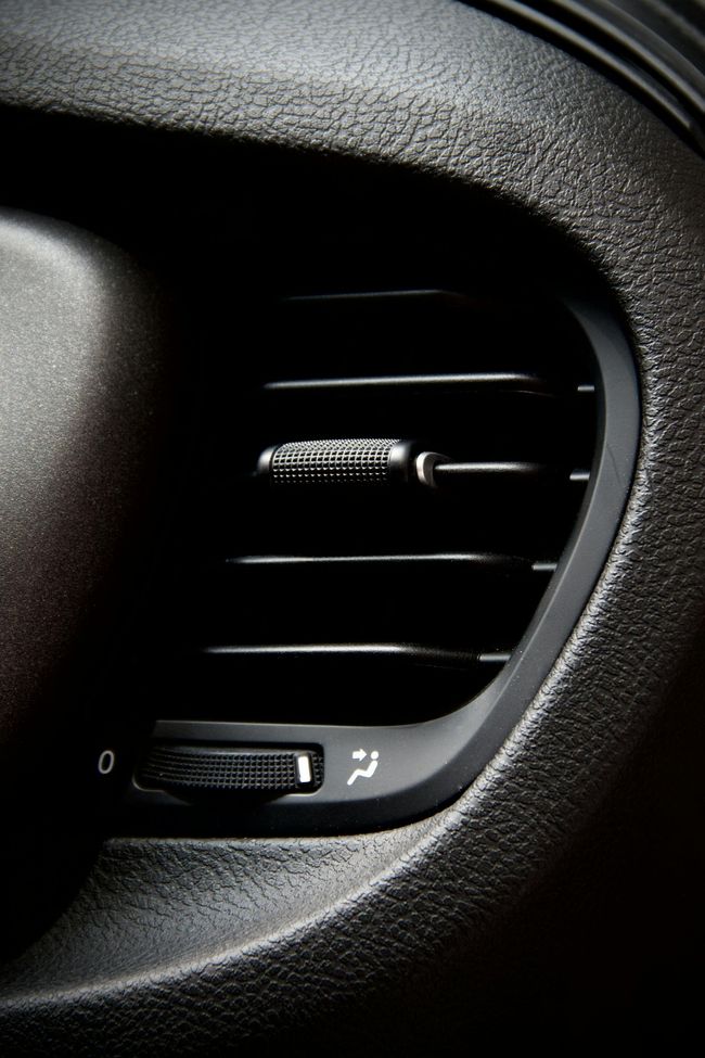 Car dashboard air vent, black plastic with adjustable fins and airflow direction control.