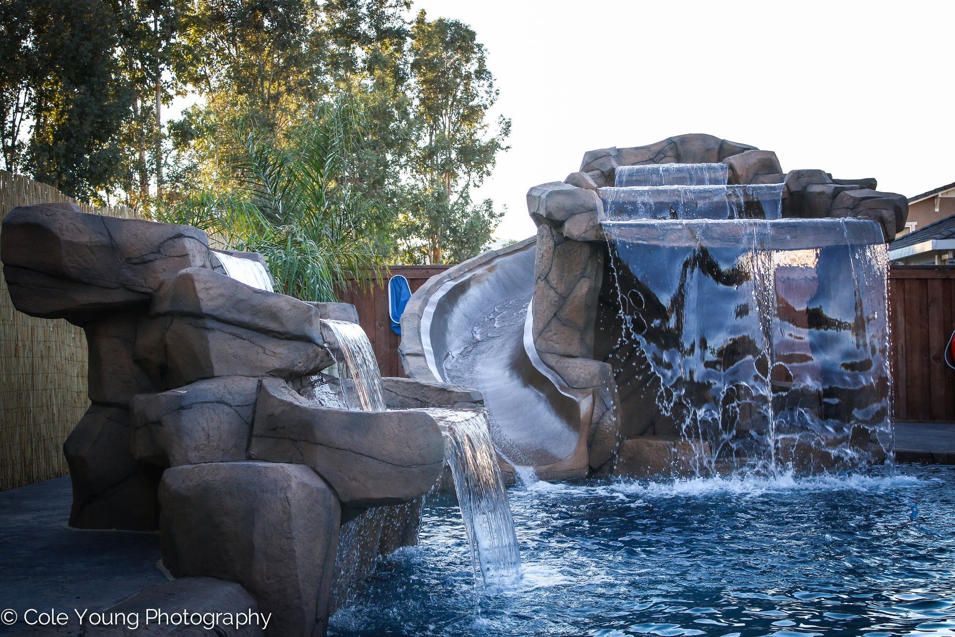 A faux-rock swimming pool feature with a tiered waterfall and a curved water slide flowing into a blue pool.