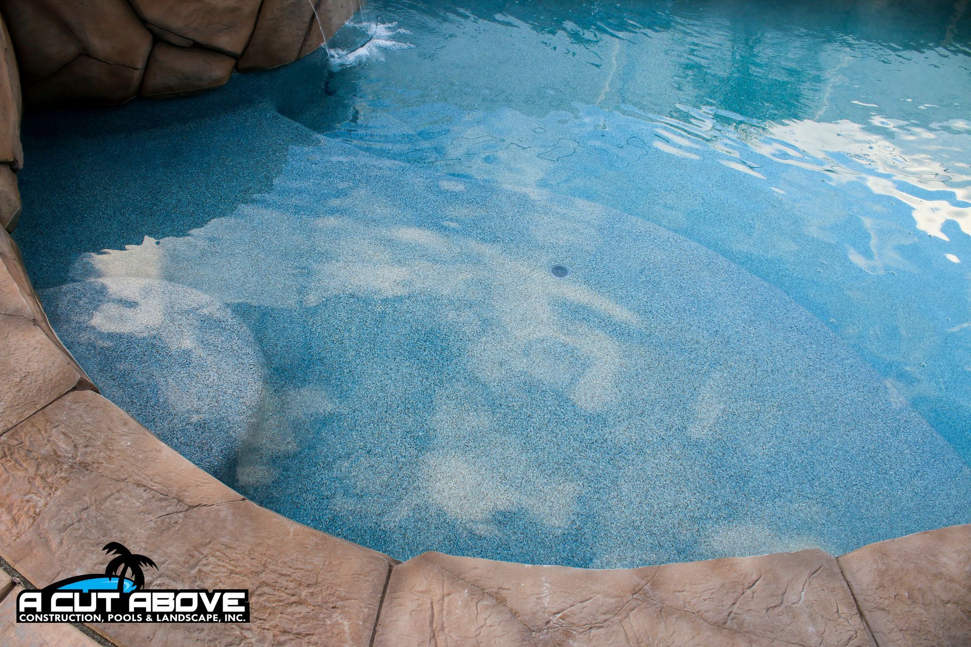A turquoise tiled pool with a stepped entry, surrounded by decorative tan stone coping.
