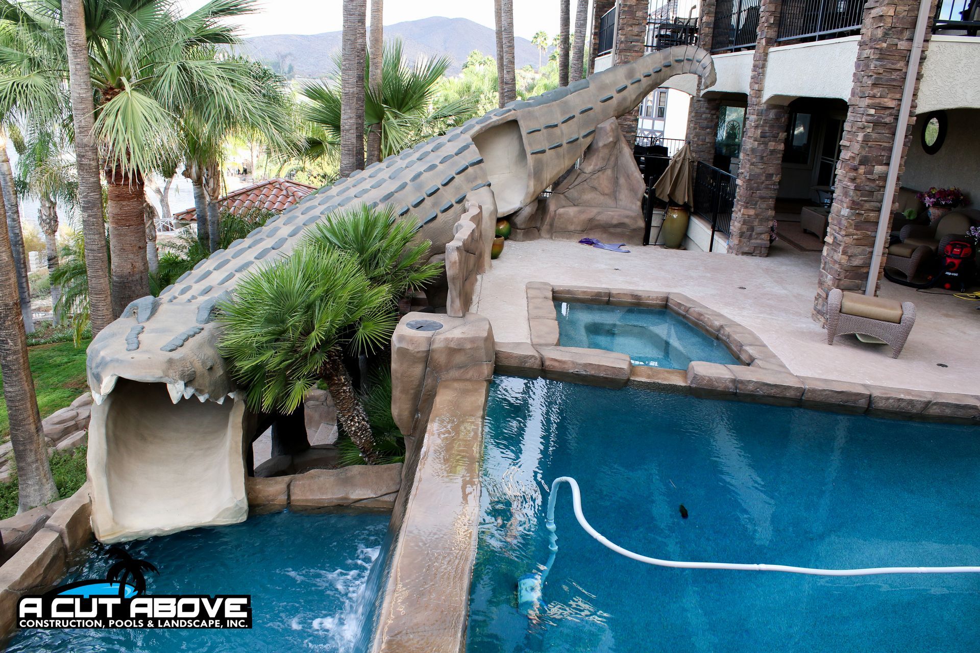 A swimming pool featuring a large, sculpted stone alligator slide that extends from a patio into the water.