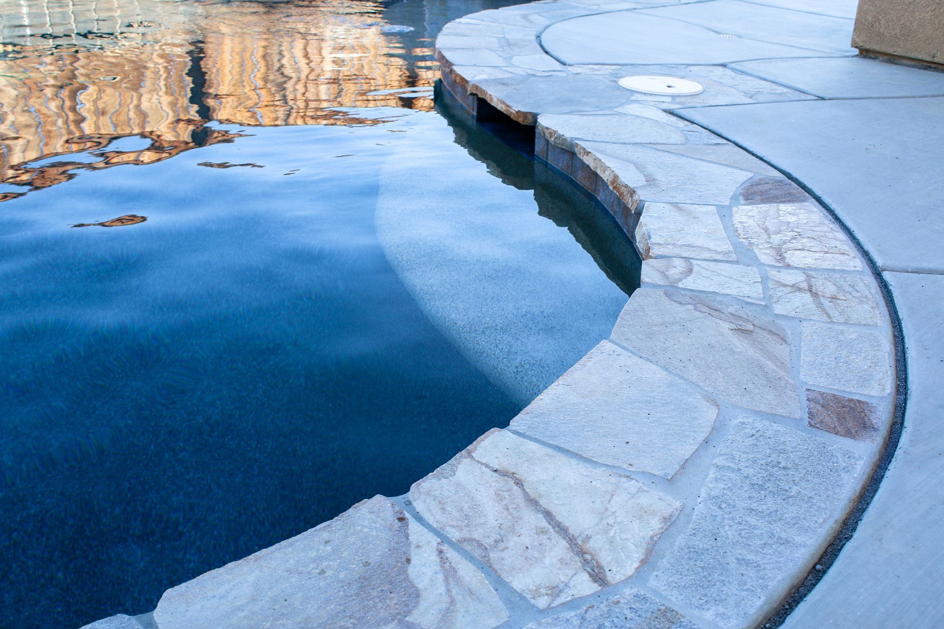 Curved stone coping bordering a deep blue swimming pool with smooth concrete decking.