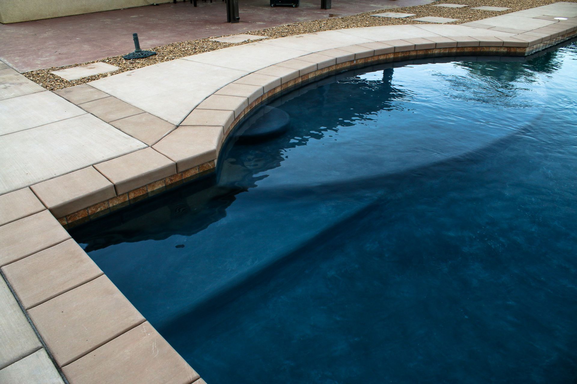 A dark blue swimming pool with curved beige tiled steps and stone decking.