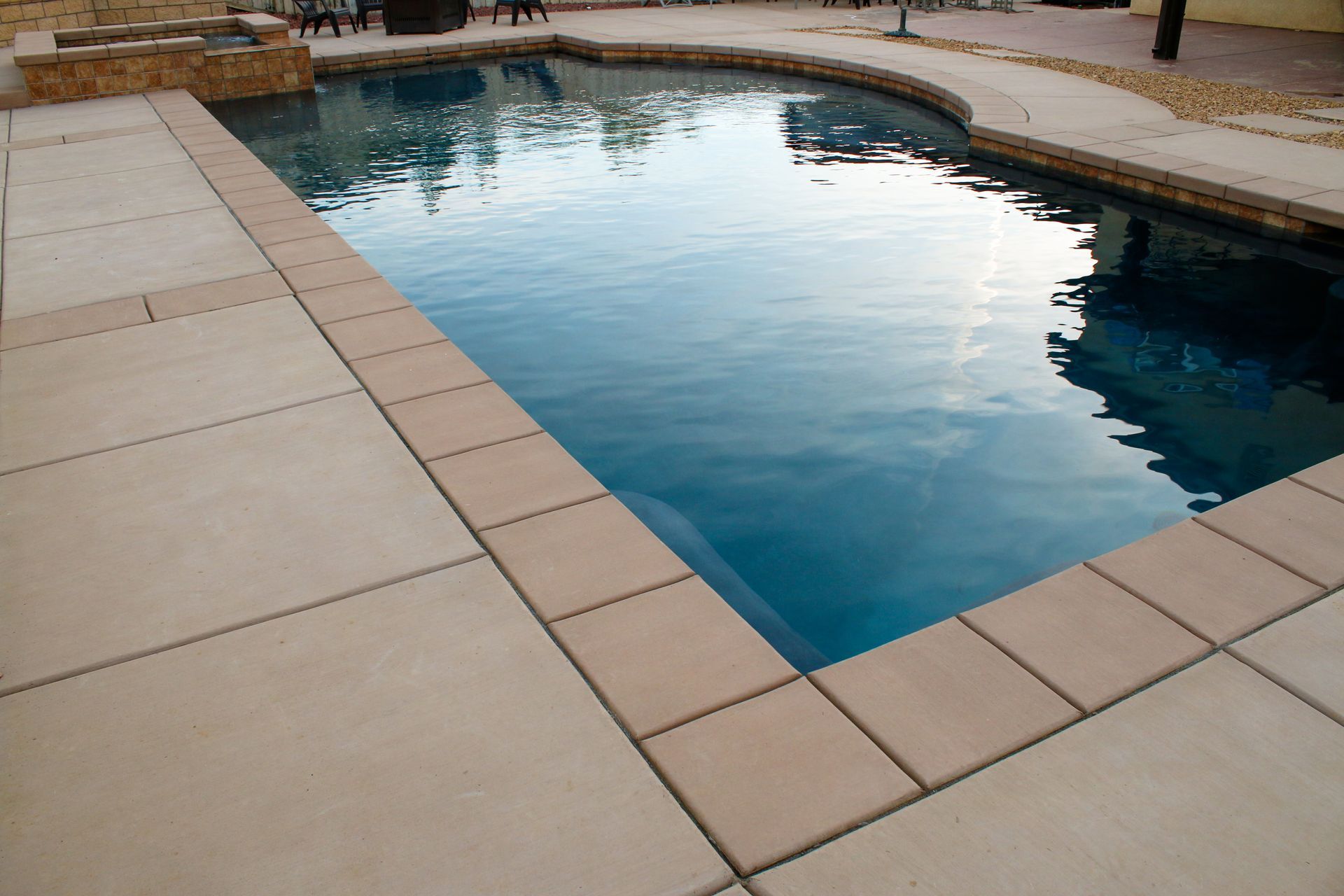 A rectangular swimming pool with deep blue water, surrounded by light-colored concrete pavers and a stone accent wall.