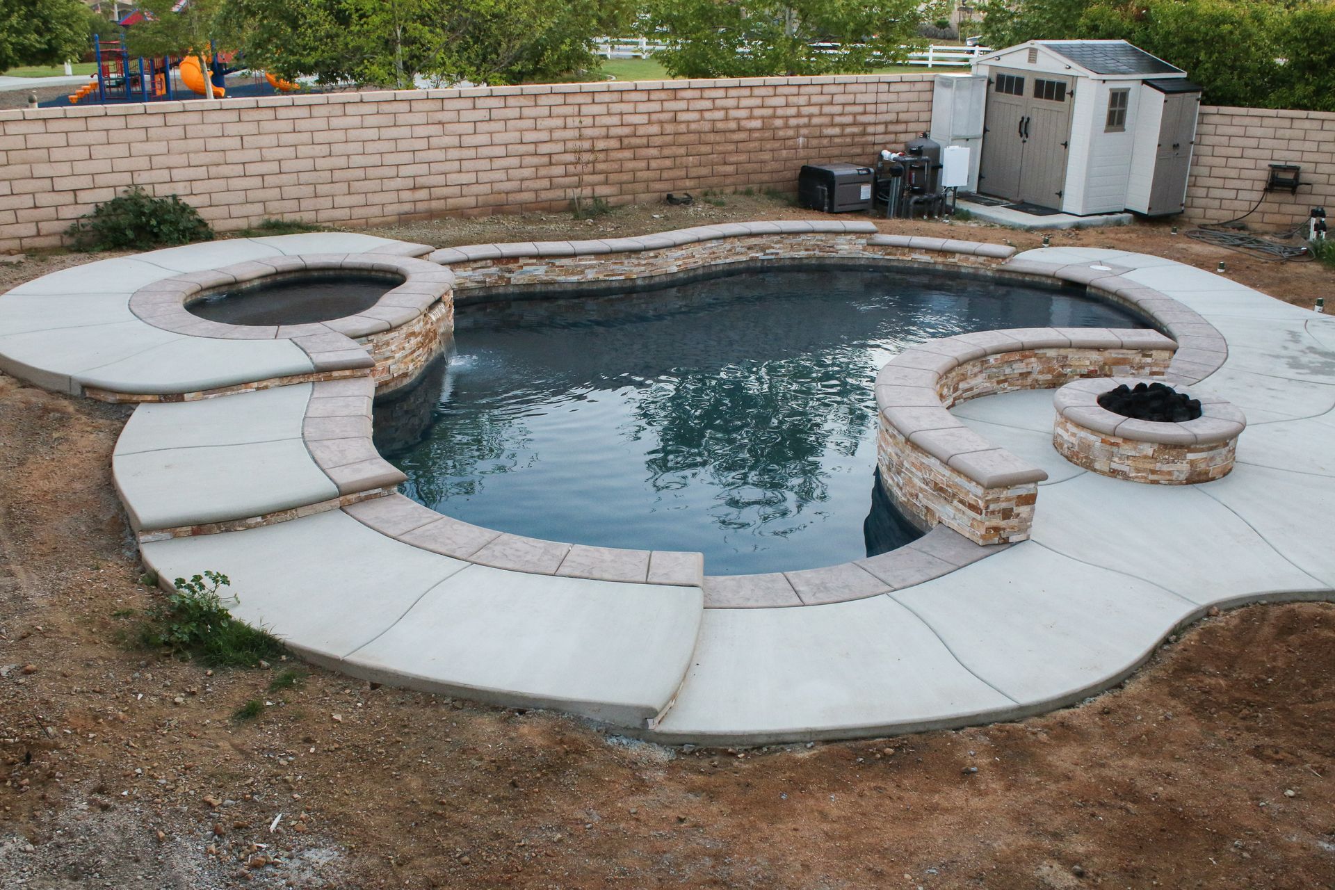 A backyard pool shaped like Mickey Mouse, featuring a built-in hot tub, a fire pit, and light-colored stone coping.