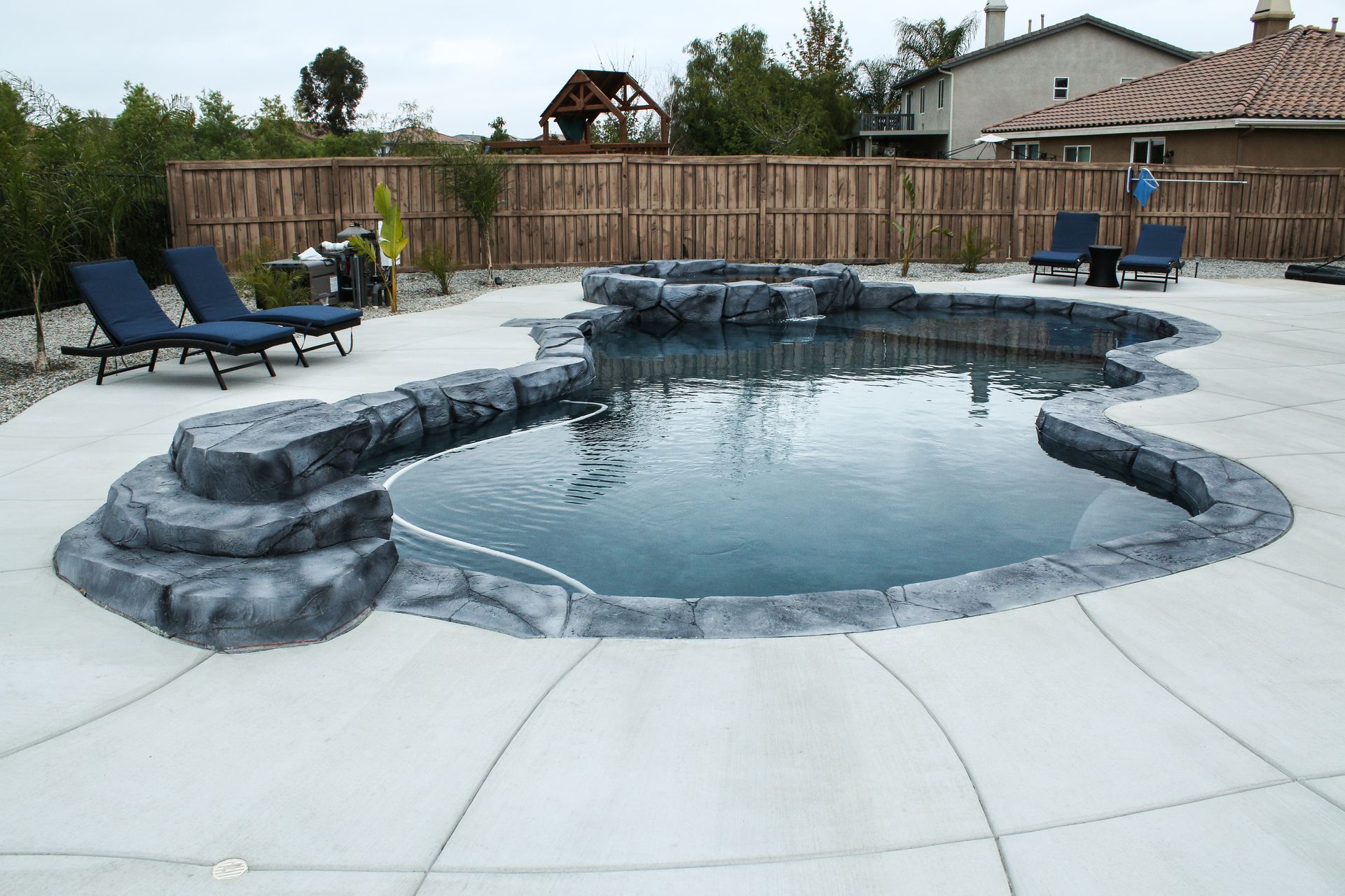A kidney-shaped swimming pool with artificial rock borders and integrated steps in a concrete backyard patio.