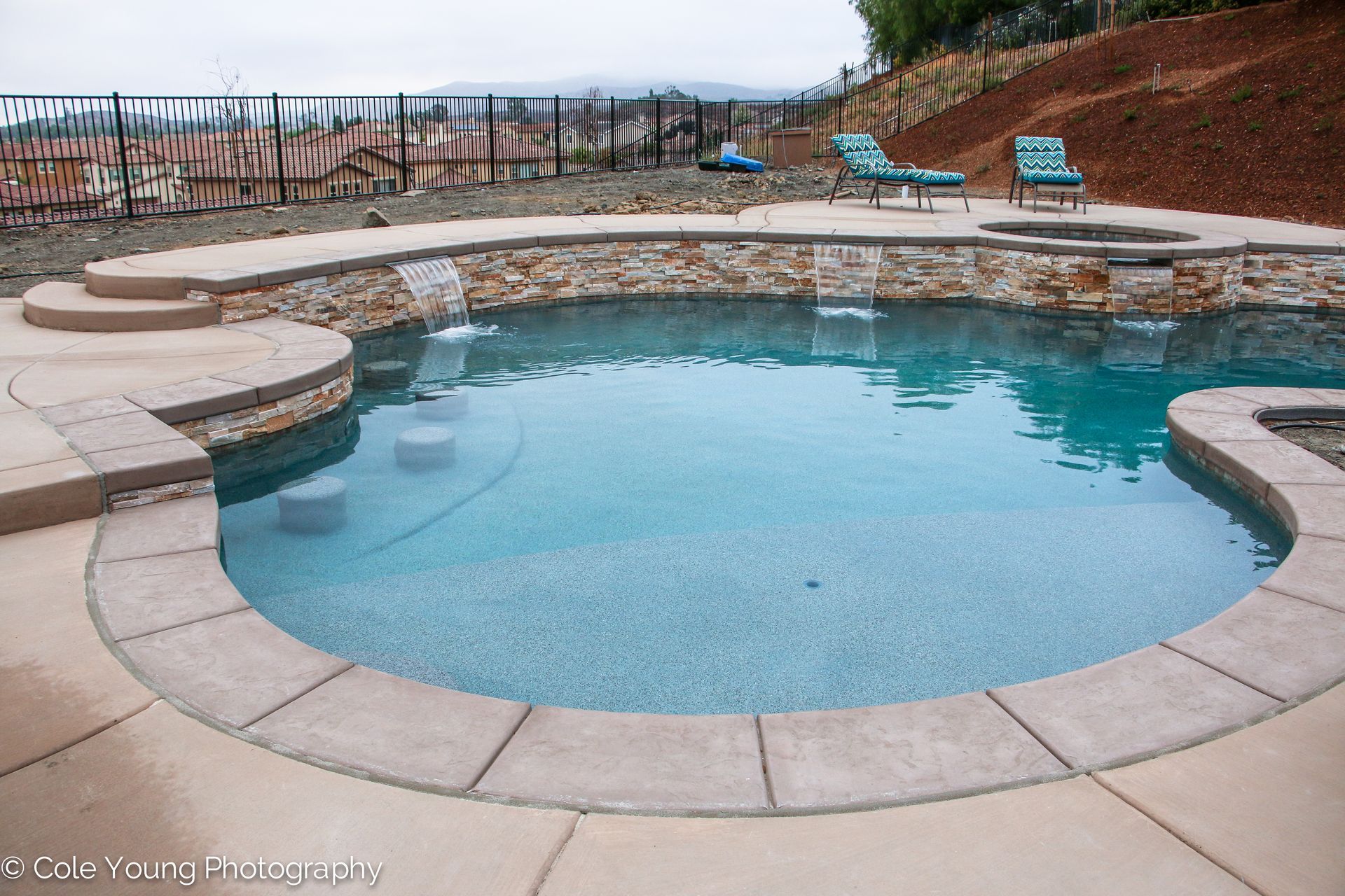 A backyard swimming pool with stone waterfall features, integrated seating, and two lounge chairs on the upper patio.