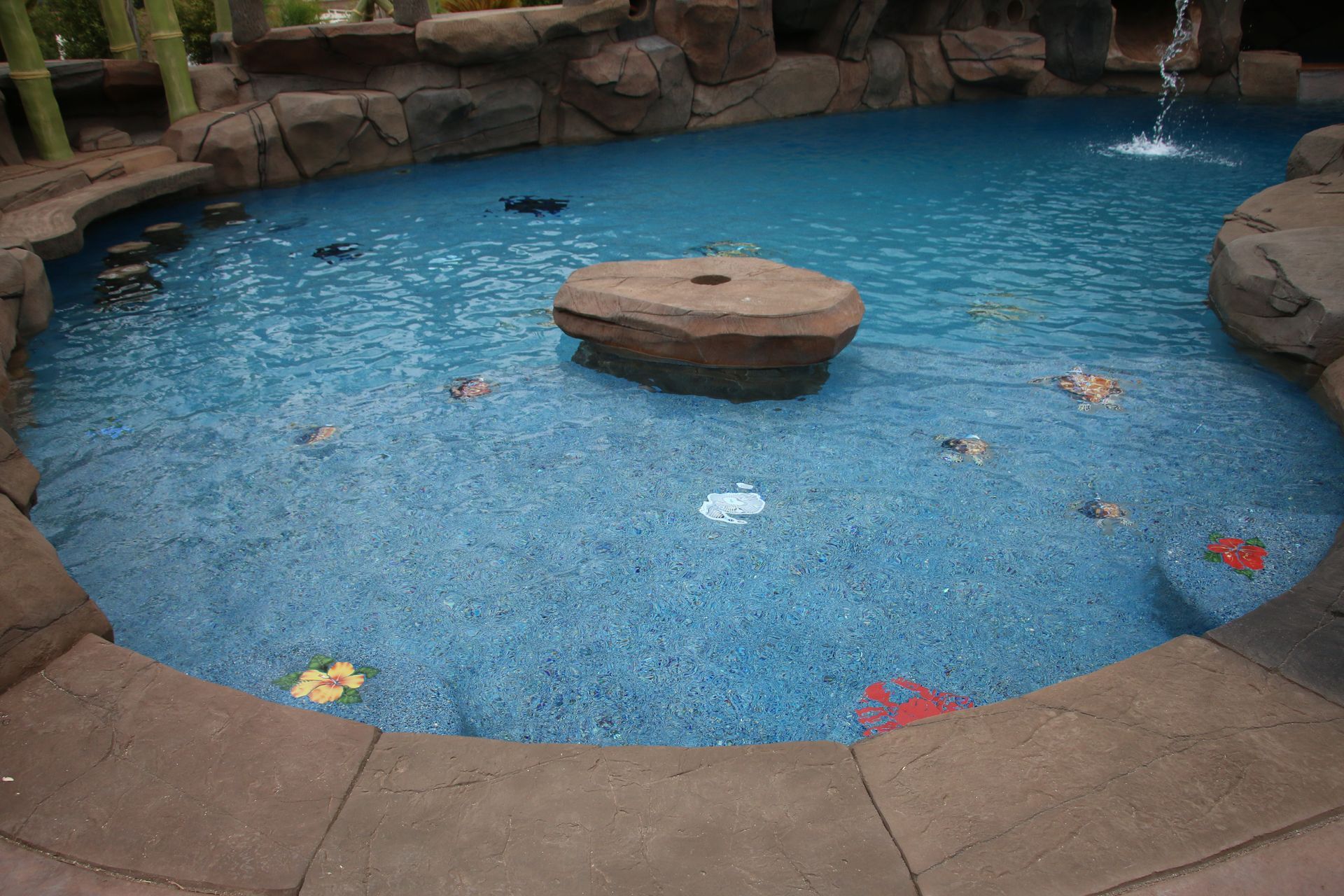 A custom backyard pool with a rock feature in the center, built-in stools, and colorful decorative tiles on the floor.