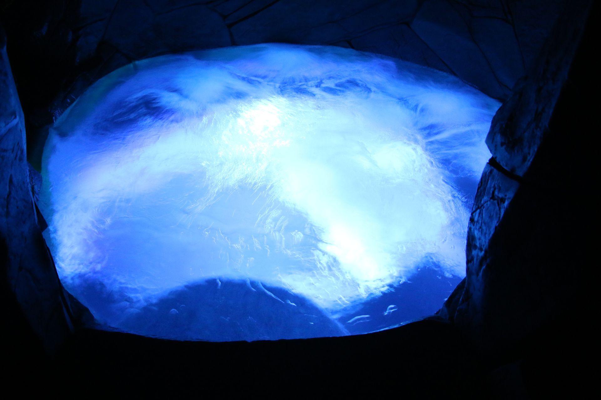 A small, dark pool of water illuminated from below with a bright, glowing blue light, creating ripples on the surface.